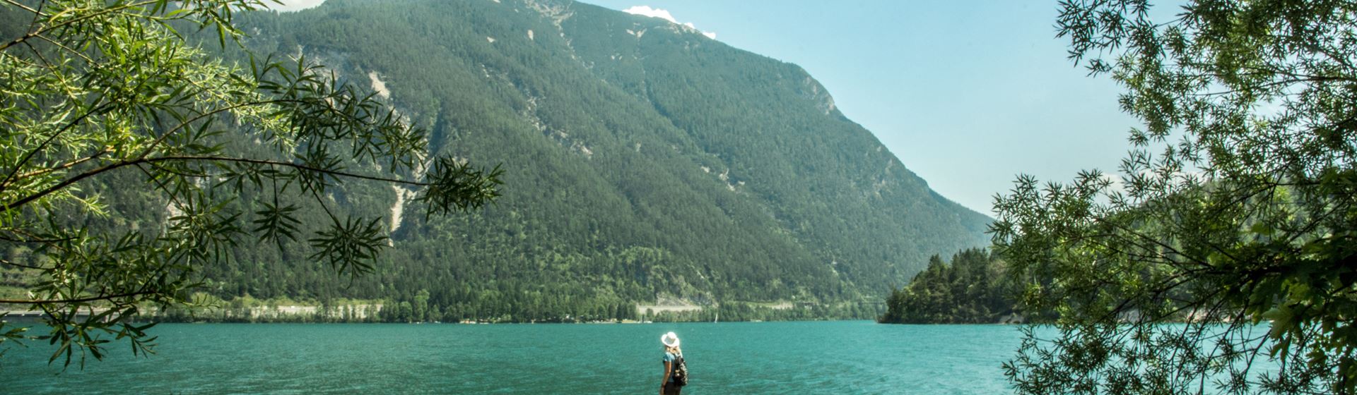 Een vrouw kijkt uit op de Achensee in Oostenrijk. Het meer is groenblauw. Op de achtergrond is een berg te zien.