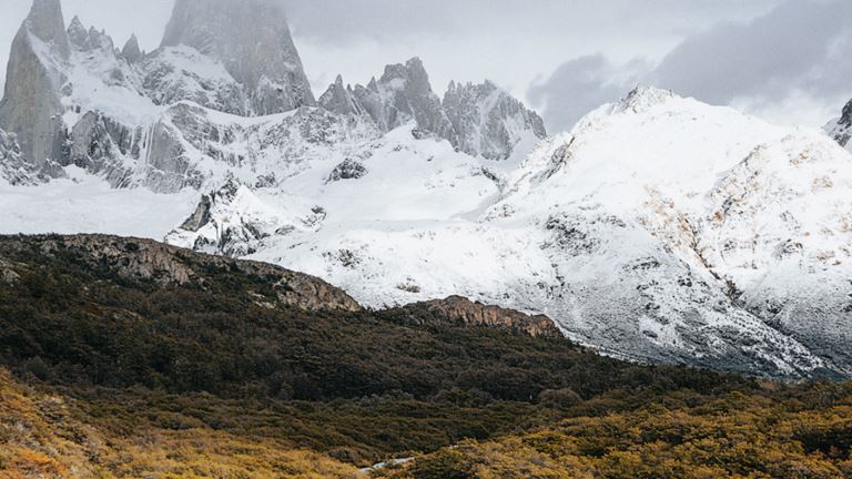Een man, op de rug gezien, kijkt vanaf een rots naar de besneeuwde berg Cerro Chaltén. 