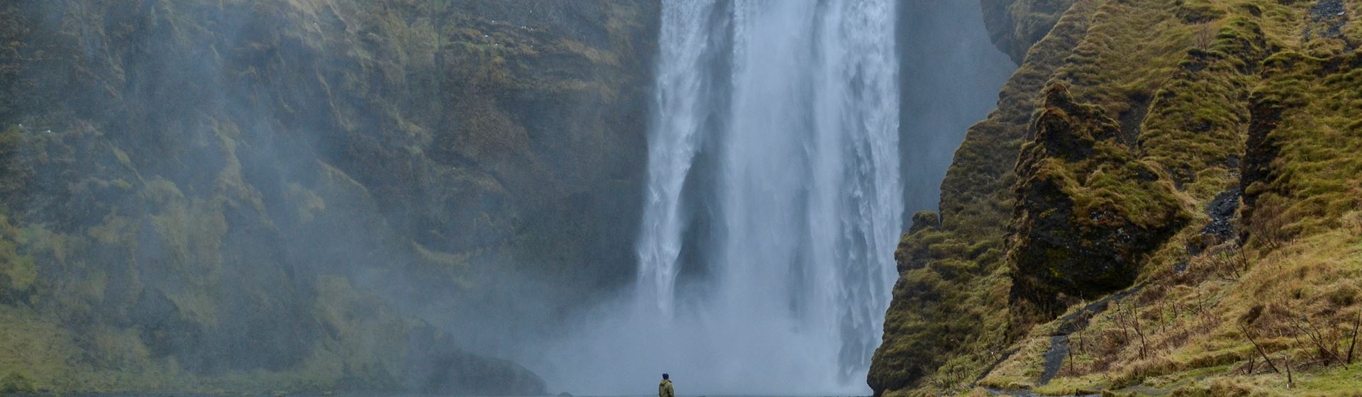 De 60 meter hoge en 25 meter brede waterval Skógafoss in het zuiden van IJsland. Voor de waterval staat een vrouw